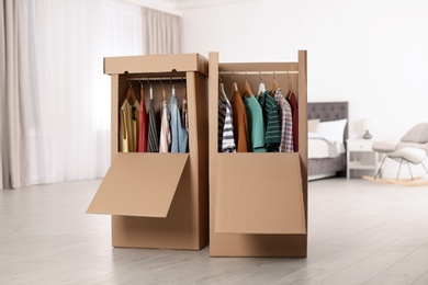 Photo of Cardboard wardrobe boxes with clothes on hangers in bedroom