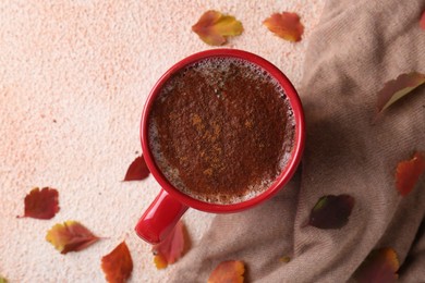 Photo of Cup of hot drink, leaves and soft knitted fabric on beige textured table, flat lay. Cozy autumn atmosphere