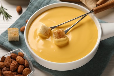 Photo of Pot of tasty cheese fondue, forks with bread pieces and almonds on white table, closeup