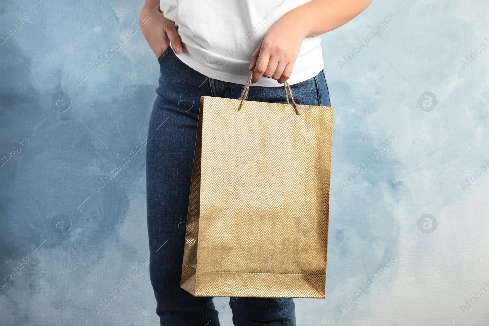 Photo of Woman with gold shopping paper bag on light blue background, closeup