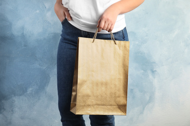 Photo of Woman with gold shopping paper bag on light blue background, closeup