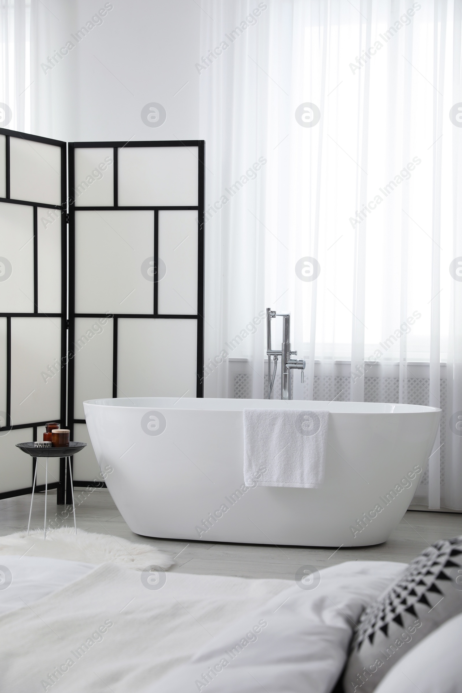 Photo of Stylish light apartment interior with white bathtub and bed