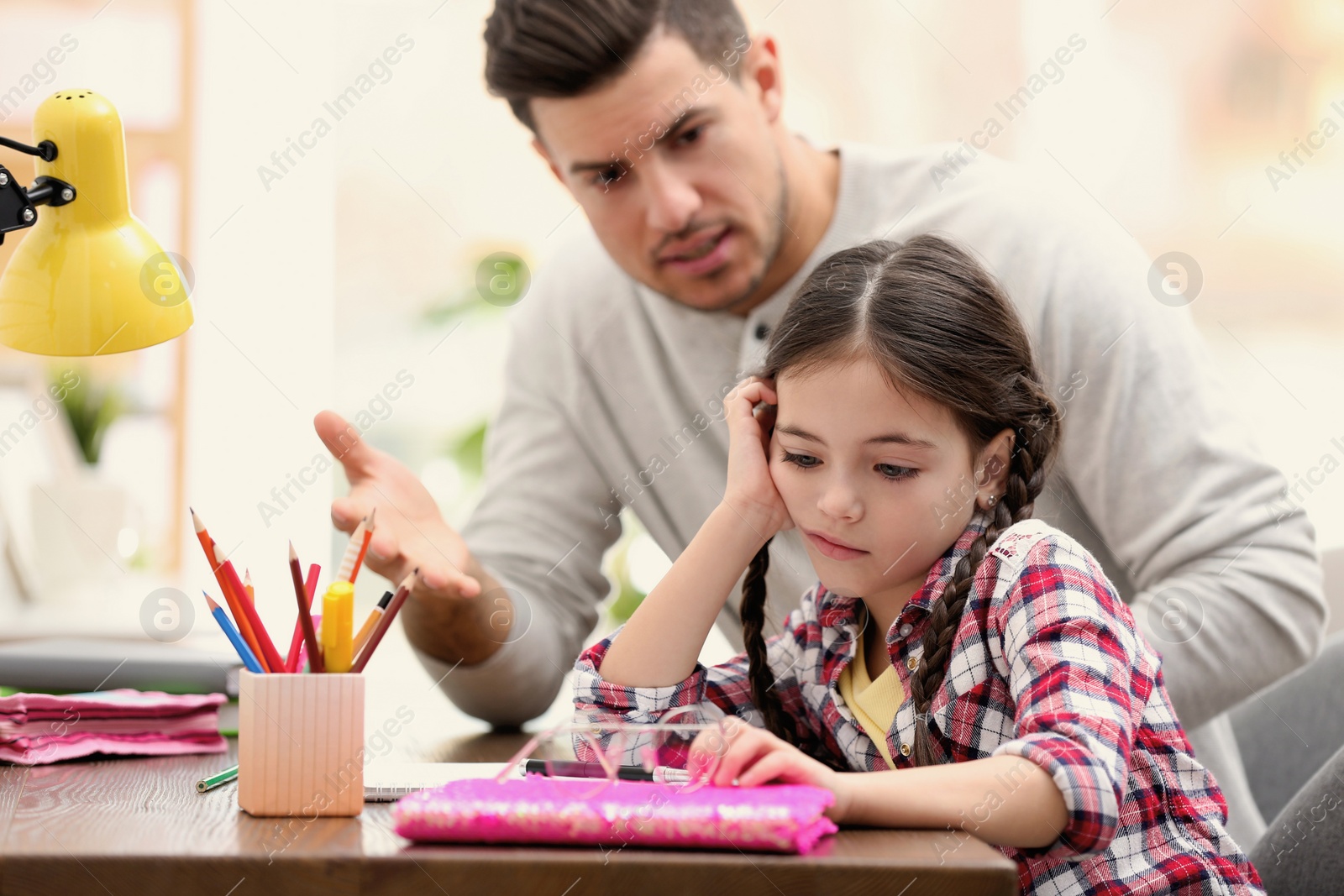 Photo of Father scolding his daughter while helping with homework at table indoors