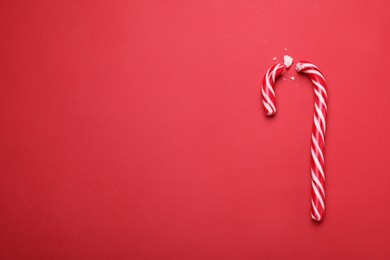 Photo of Broken sweet Christmas candy cane on red background, top view. Space for text