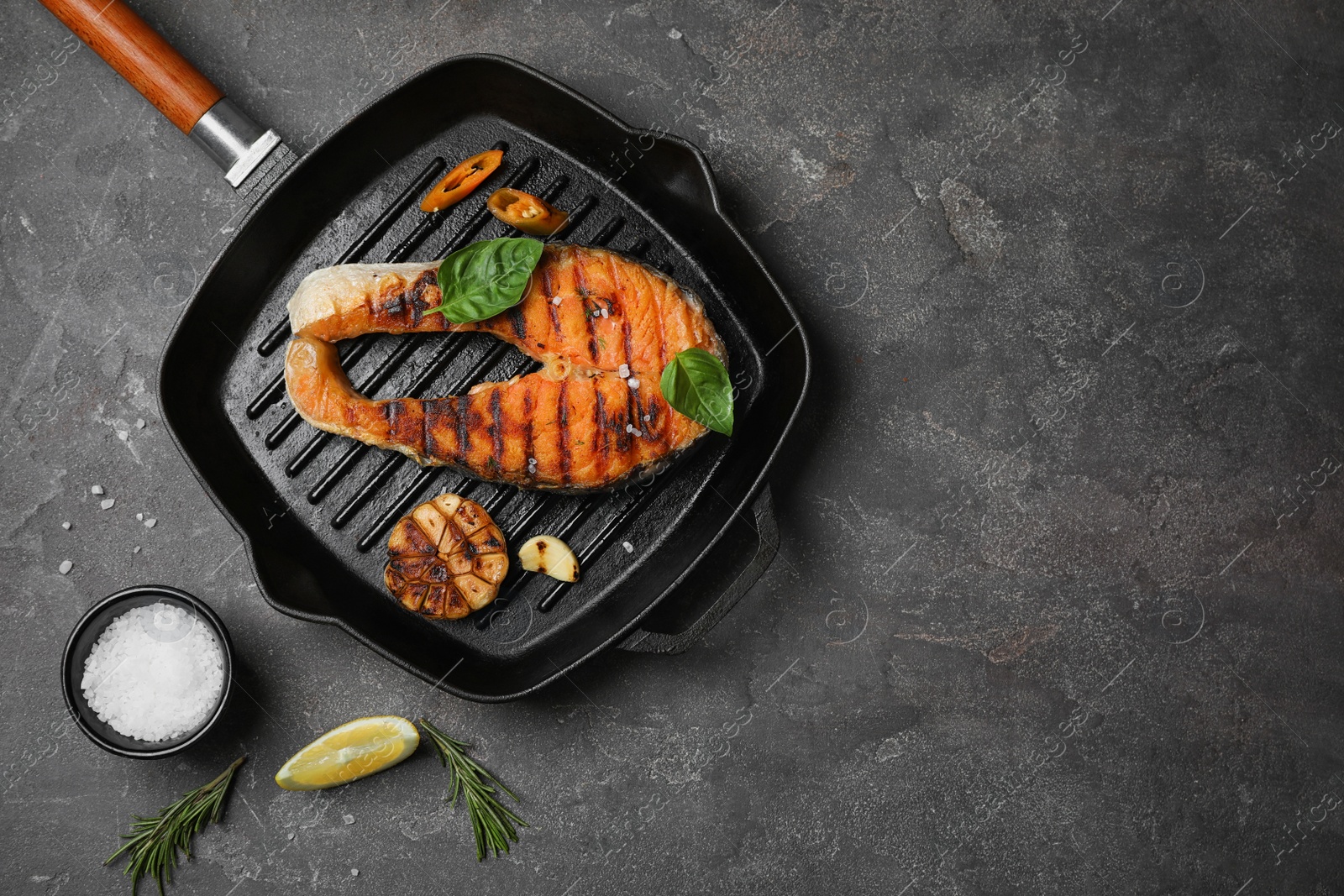 Photo of Frying pan with tasty salmon steak on grey background