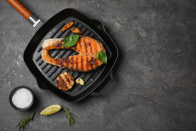 Frying pan with tasty salmon steak on grey background