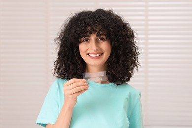 Photo of Young woman holding teeth whitening strips indoors