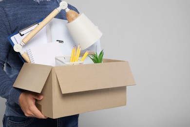 Photo of Unemployed man with box of personal office belongings on light grey background, closeup. Space for text