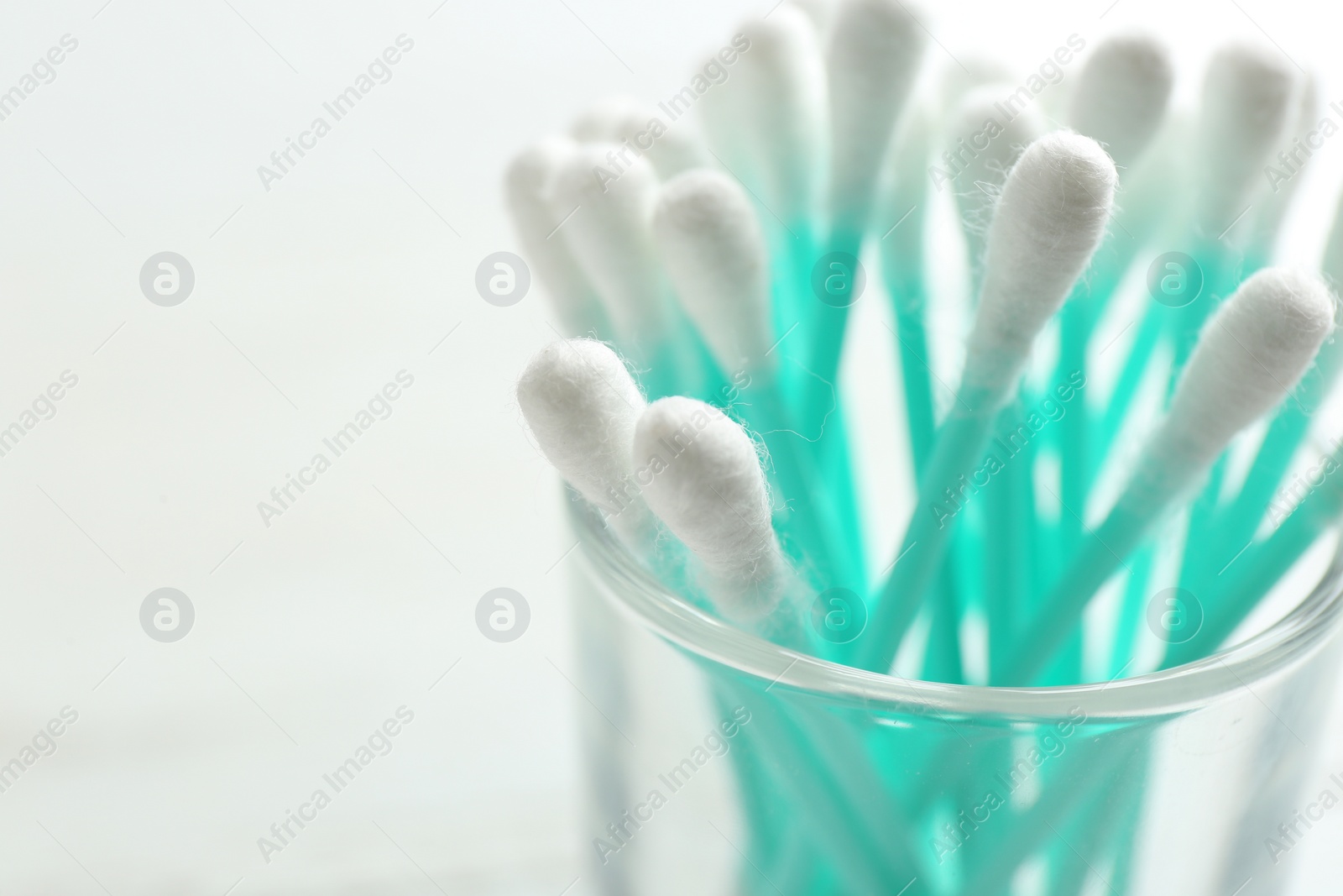 Photo of Glass with cotton swabs on light background, closeup. Space for text