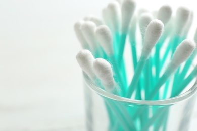 Glass with cotton swabs on light background, closeup. Space for text