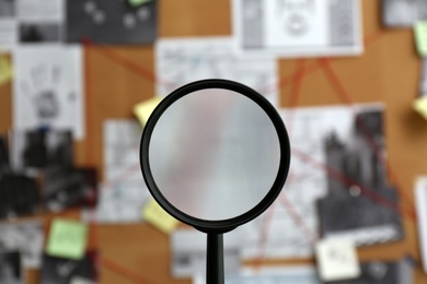 Magnifying glass and blurred detective board, closeup