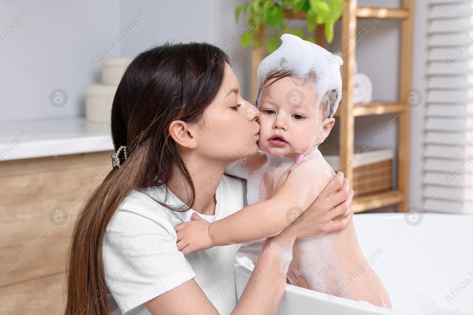 Photo of Mother bathing her cute little baby in tub at home