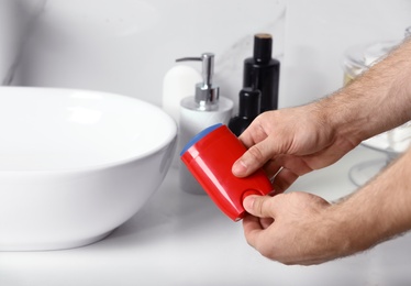 Photo of Man holding stick deodorant in bathroom, closeup view. Space for text