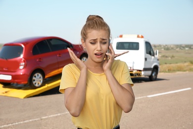 Photo of Woman talking on phone near tow truck with broken car outdoors