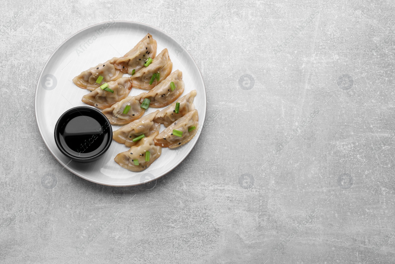 Photo of Delicious gyoza (asian dumplings) with green onions and soy sauce on light gray table, top view. Space for text