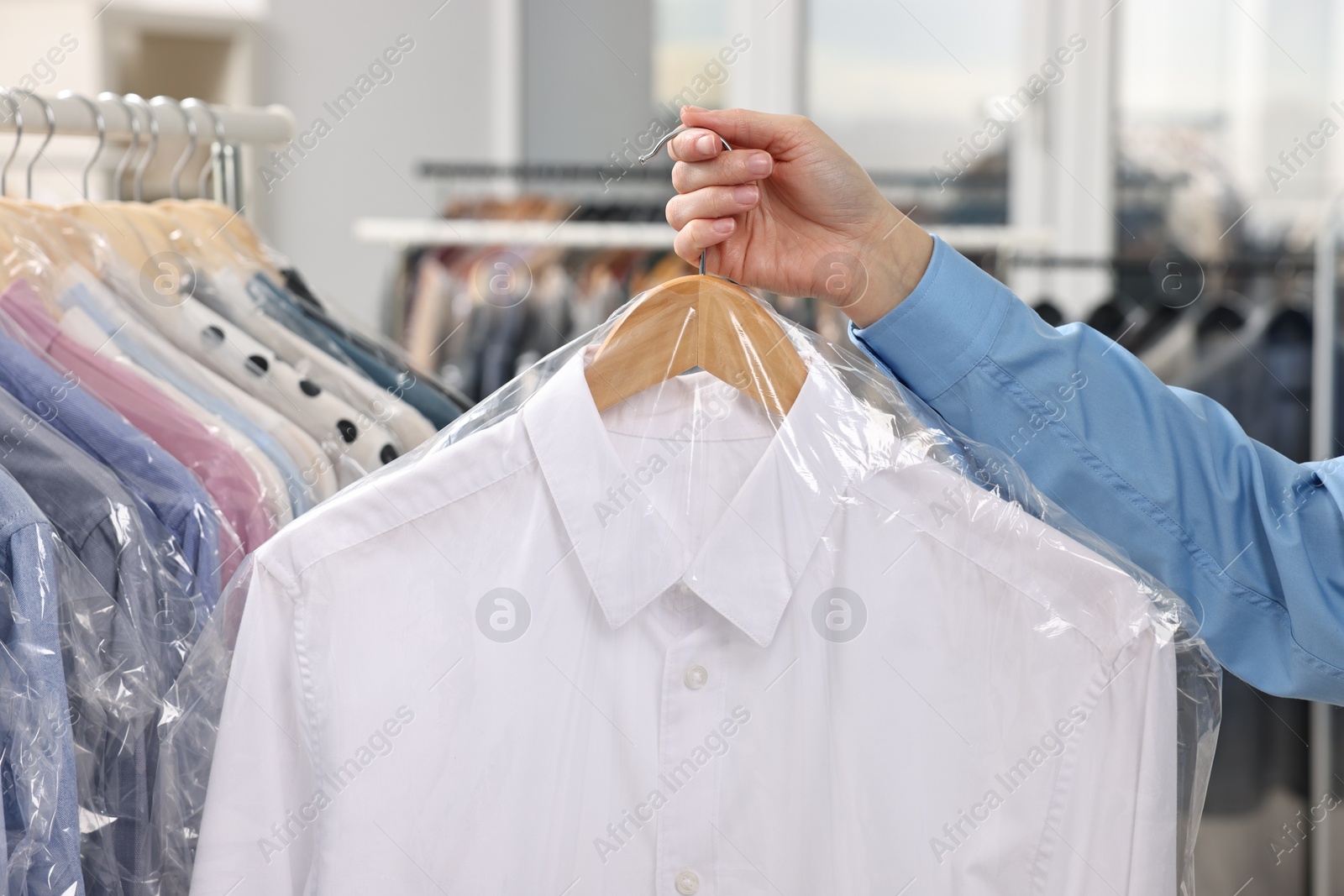 Photo of Dry-cleaning service. Woman holding shirt in plastic bag indoors, closeup