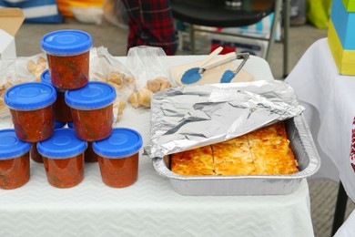 Volunteer food distribution. Containers with tasty adjika sauce near pie served on table outdoors