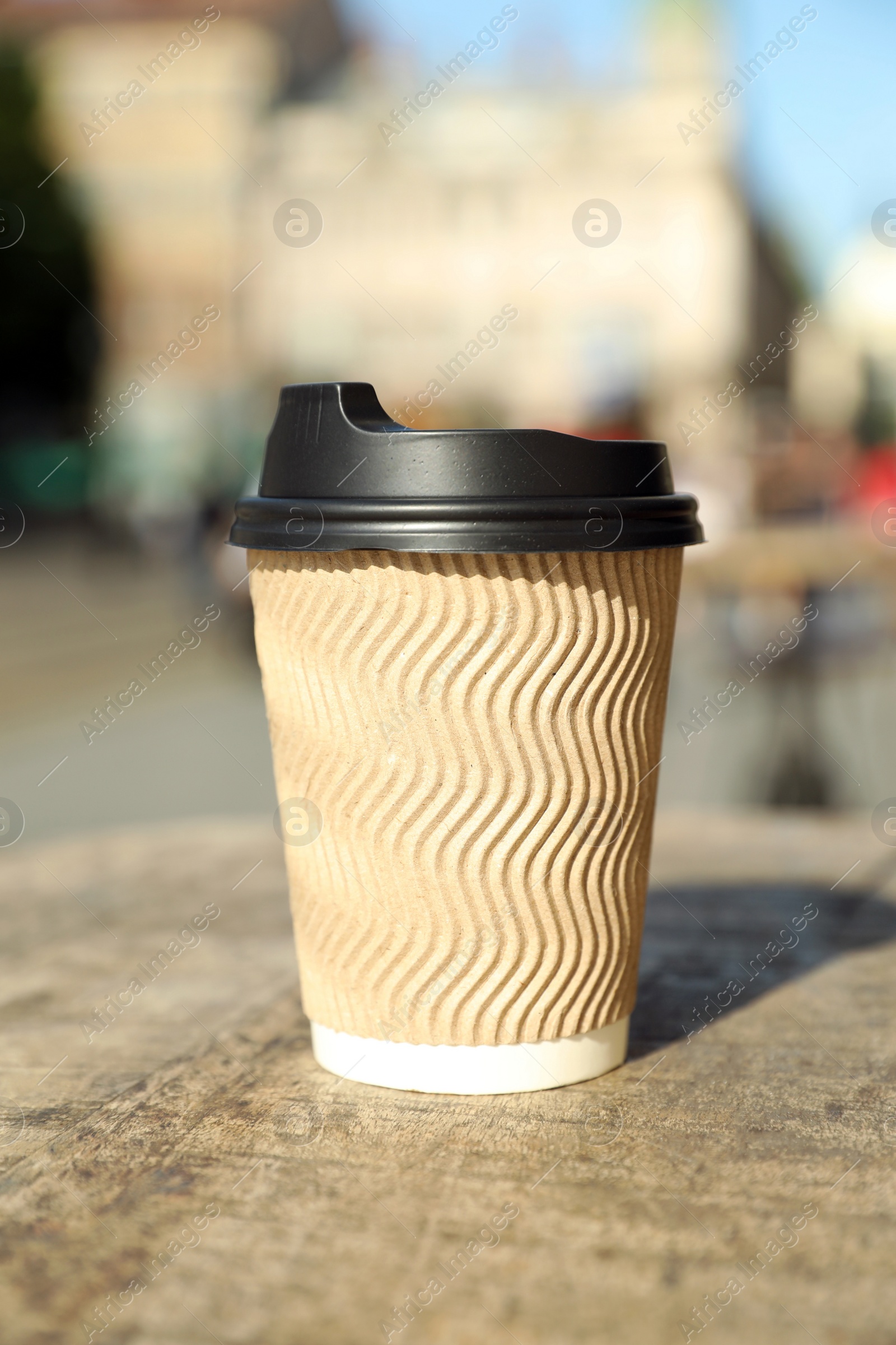 Photo of Cardboard takeaway coffee cup with plastic lid on wooden table in city