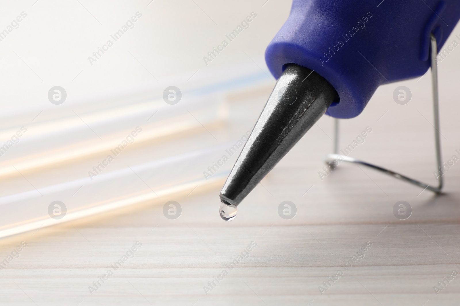 Photo of Melted glue dripping from hot gun on white table, closeup. Space for text