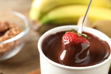 Photo of Dipping strawberry into fondue pot with chocolate, closeup