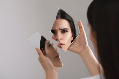 Young woman looking at herself in shard of broken mirror on light grey background, closeup