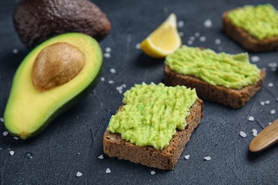 Photo of Crisp rye toasts with avocado on dark table