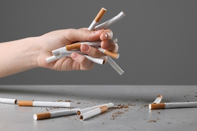 Photo of Stop smoking concept. Woman holding cigarettes above gray table, closeup