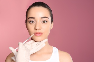 Young woman getting lip injection on color background