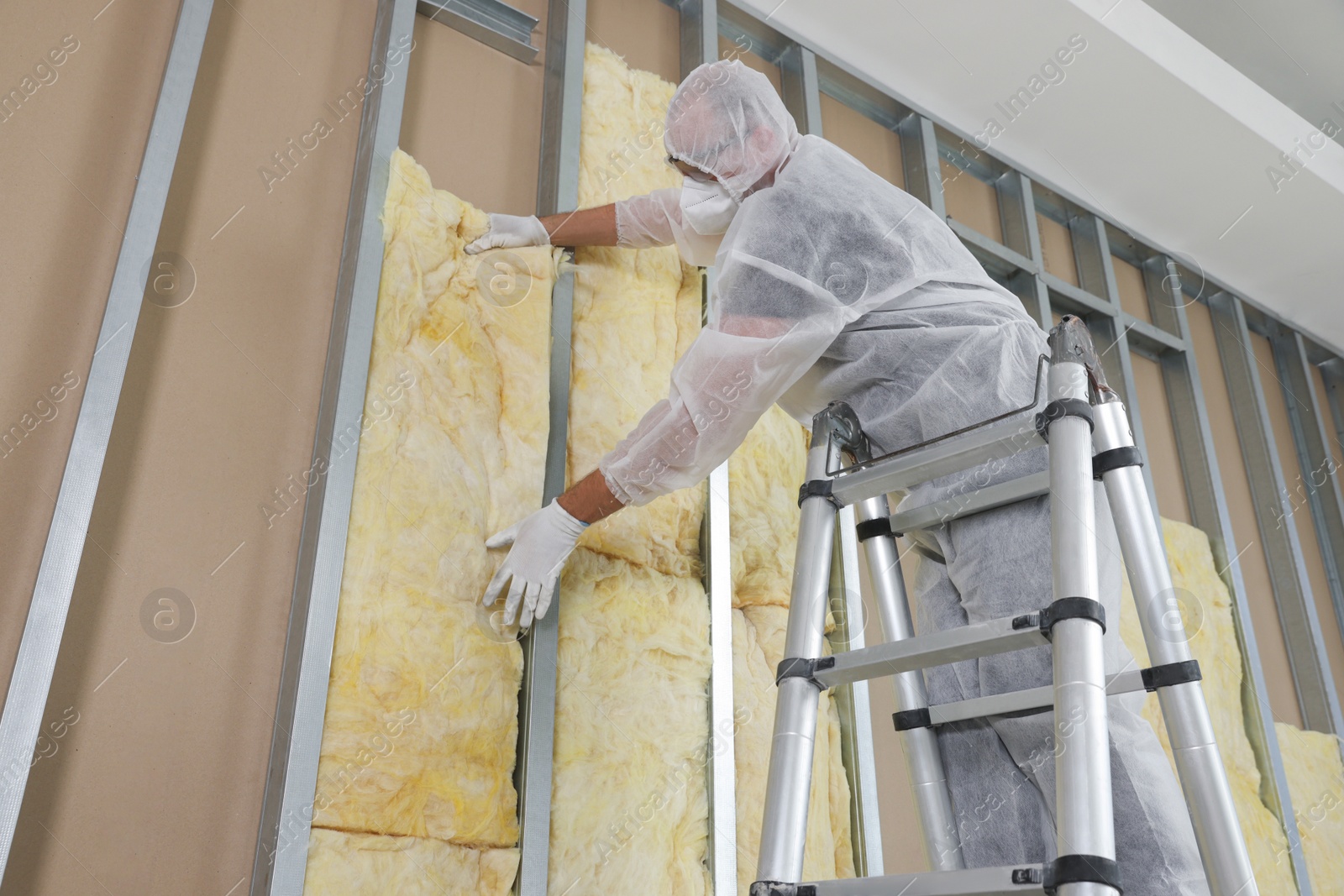 Photo of Worker insulating wall using ladder indoors, low angle view