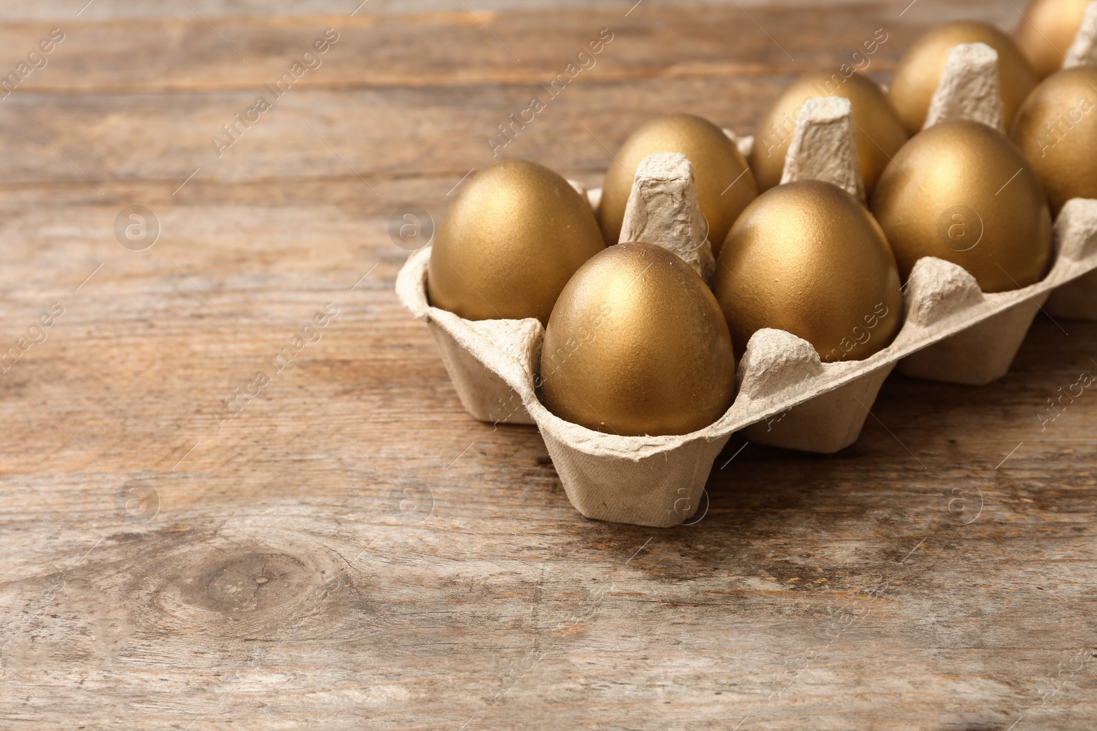 Photo of Carton with golden eggs on wooden table, space for text