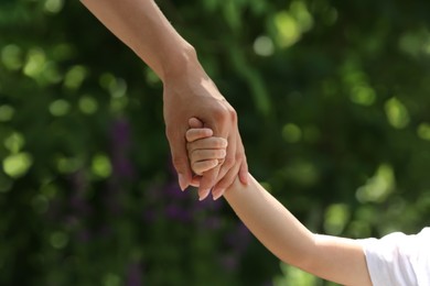 Photo of Mom and her child holding hands in park, closeup