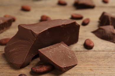 Photo of Pieces of tasty milk chocolate and cocoa beans on wooden table, closeup