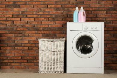 Photo of Modern washing machine with detergent and laundry basket near brick wall