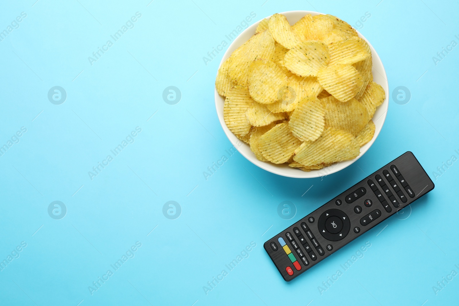 Photo of Remote control and bowl of potato chips on light blue background, flat lay. Space for text
