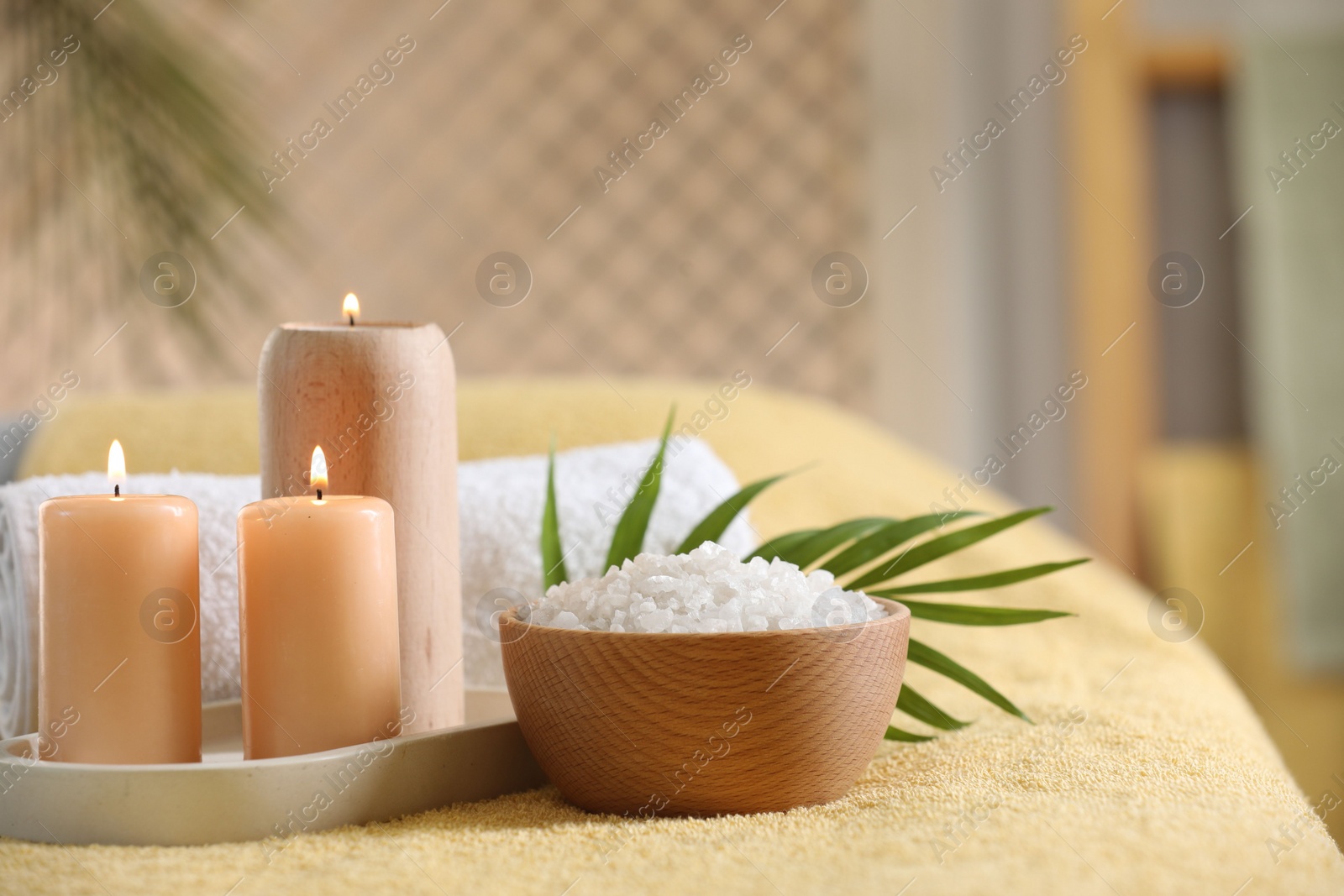 Photo of Spa composition. Burning candles, sea salt and towel on soft yellow surface, space for text