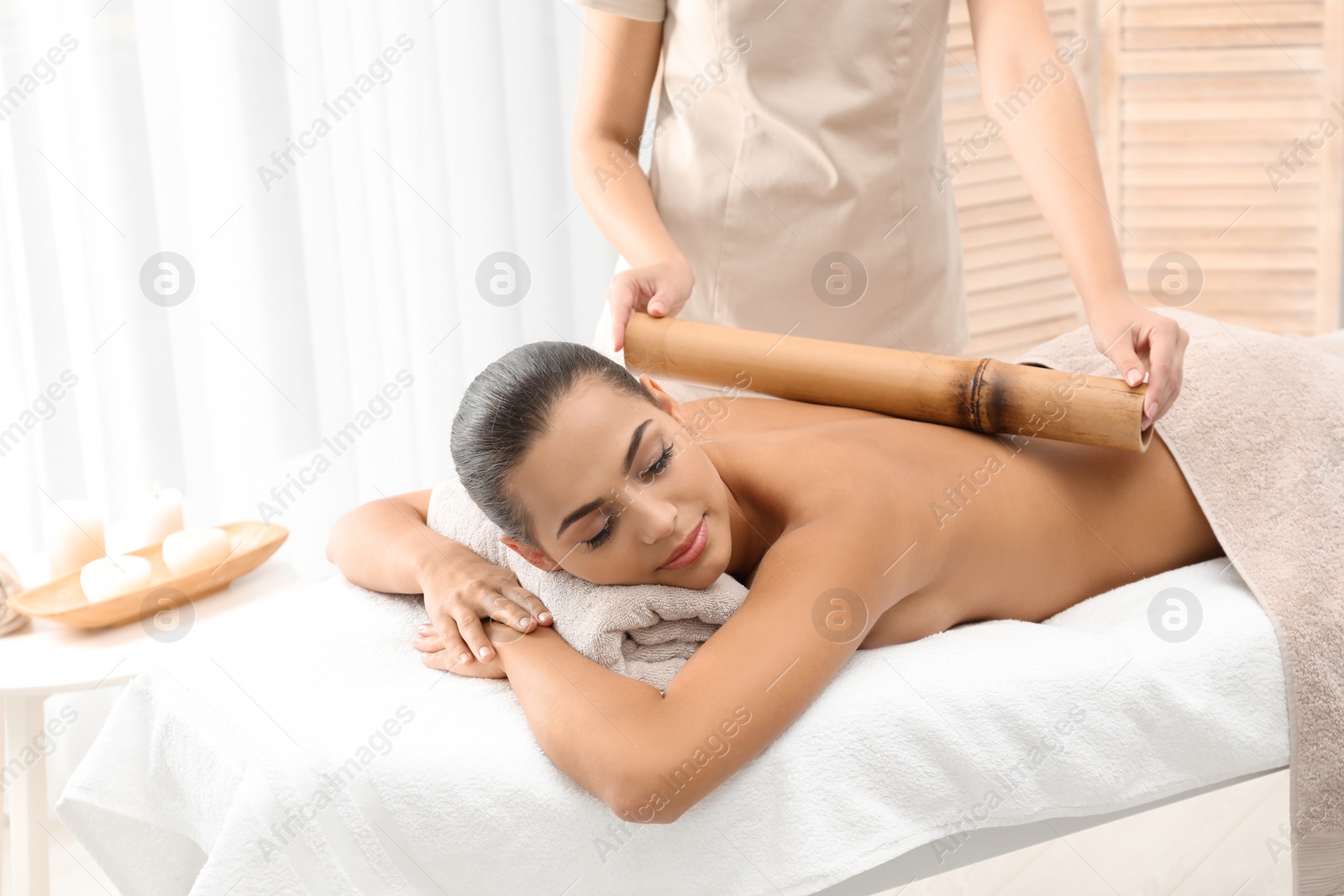 Photo of Young woman having massage with bamboo stick in wellness center