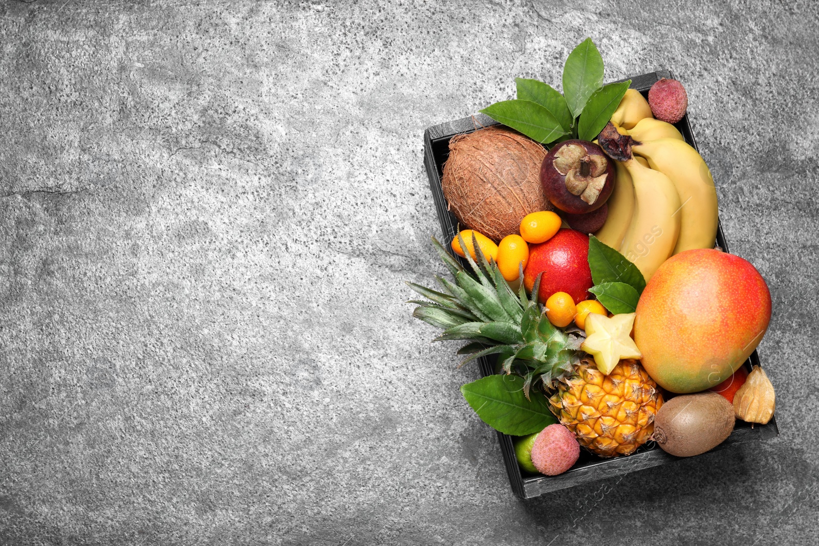 Photo of Different tropical fruits in wooden box on grey background, top view. Space for text