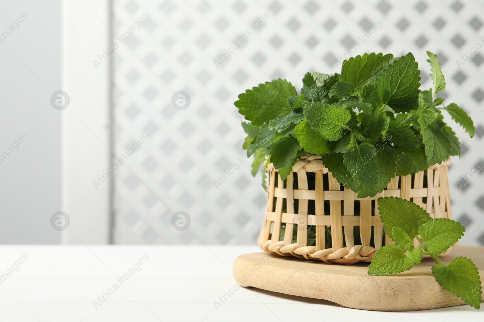 Photo of Fresh lemon balm in wicker basket on white table, space for text