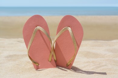 Photo of Stylish pink flip flops in sand near sea on sunny day