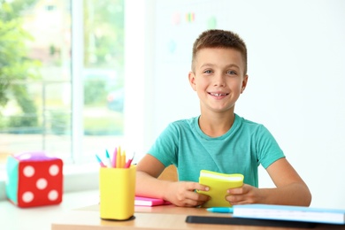 Photo of Little boy with school stationery at desk in classroom