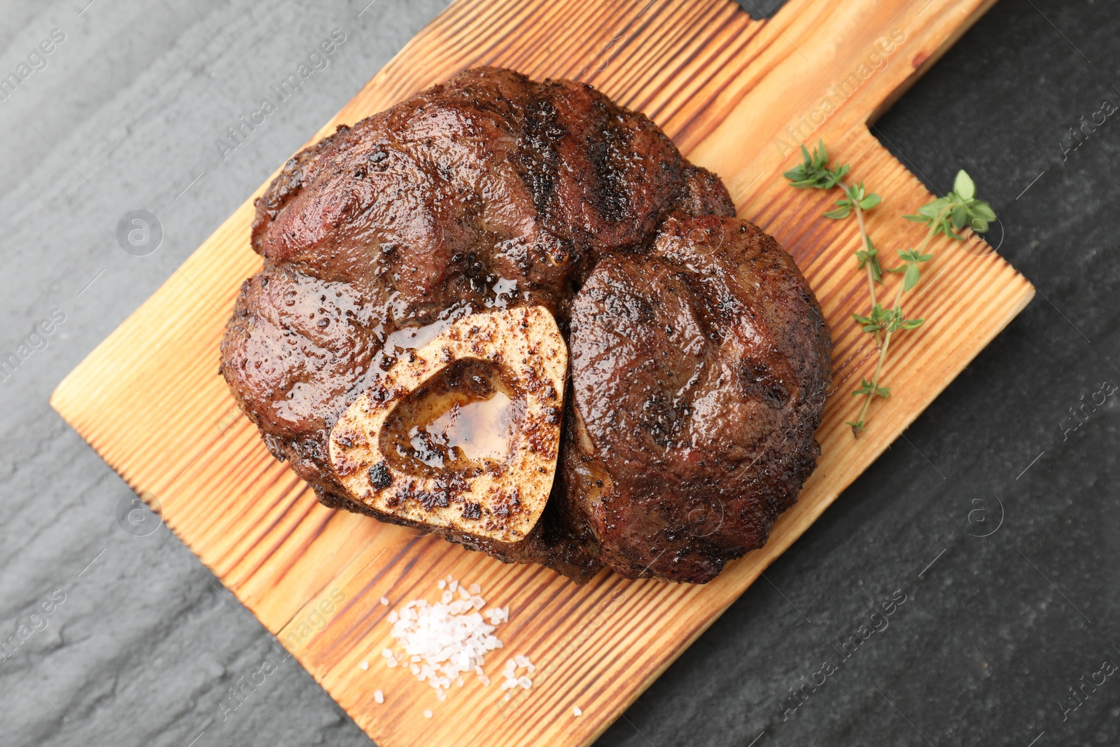 Photo of Piece of delicious grilled beef meat, thyme and salt on black table, top view