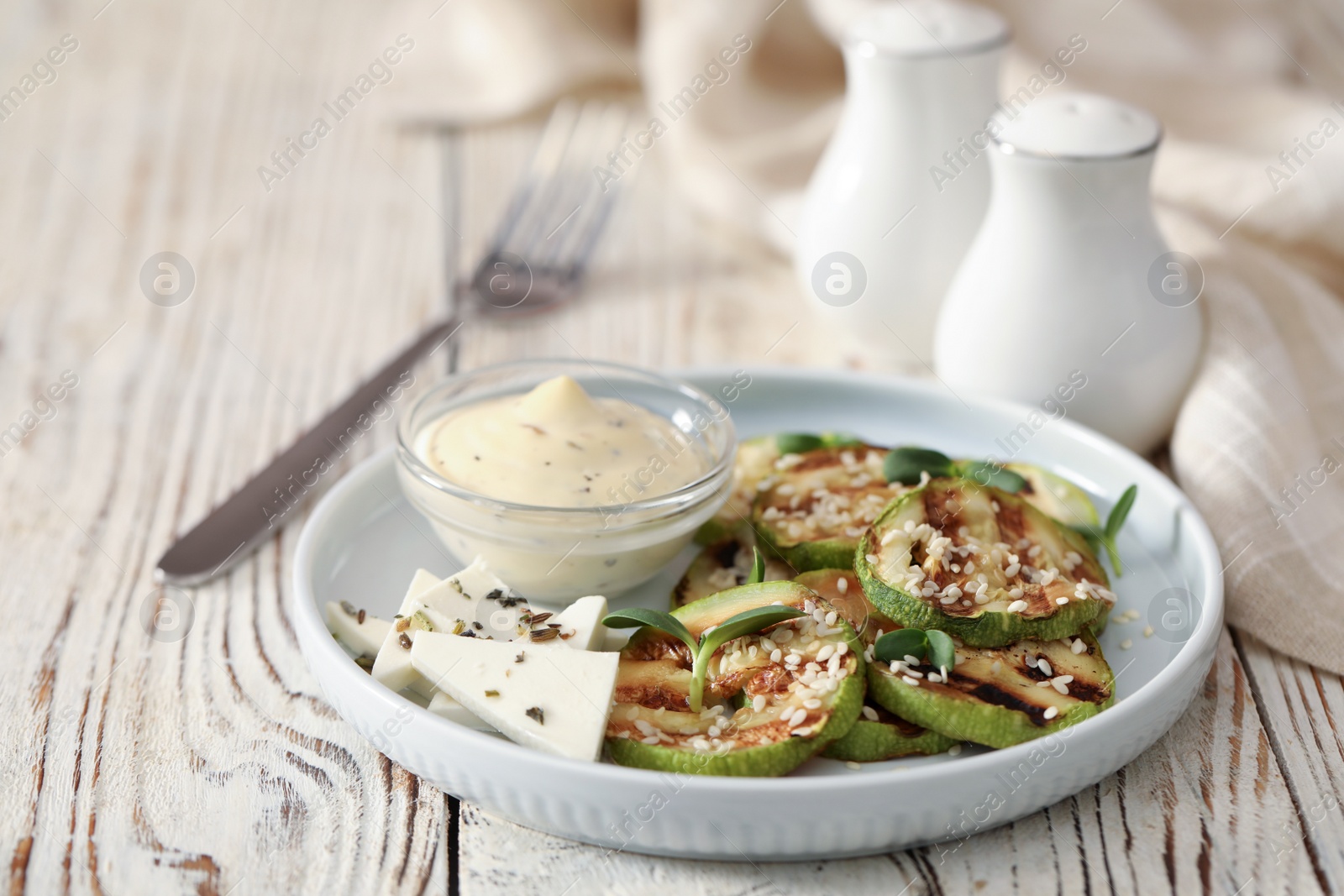 Photo of Delicious grilled zucchini slices served with sauce and cheese on white wooden table, closeup