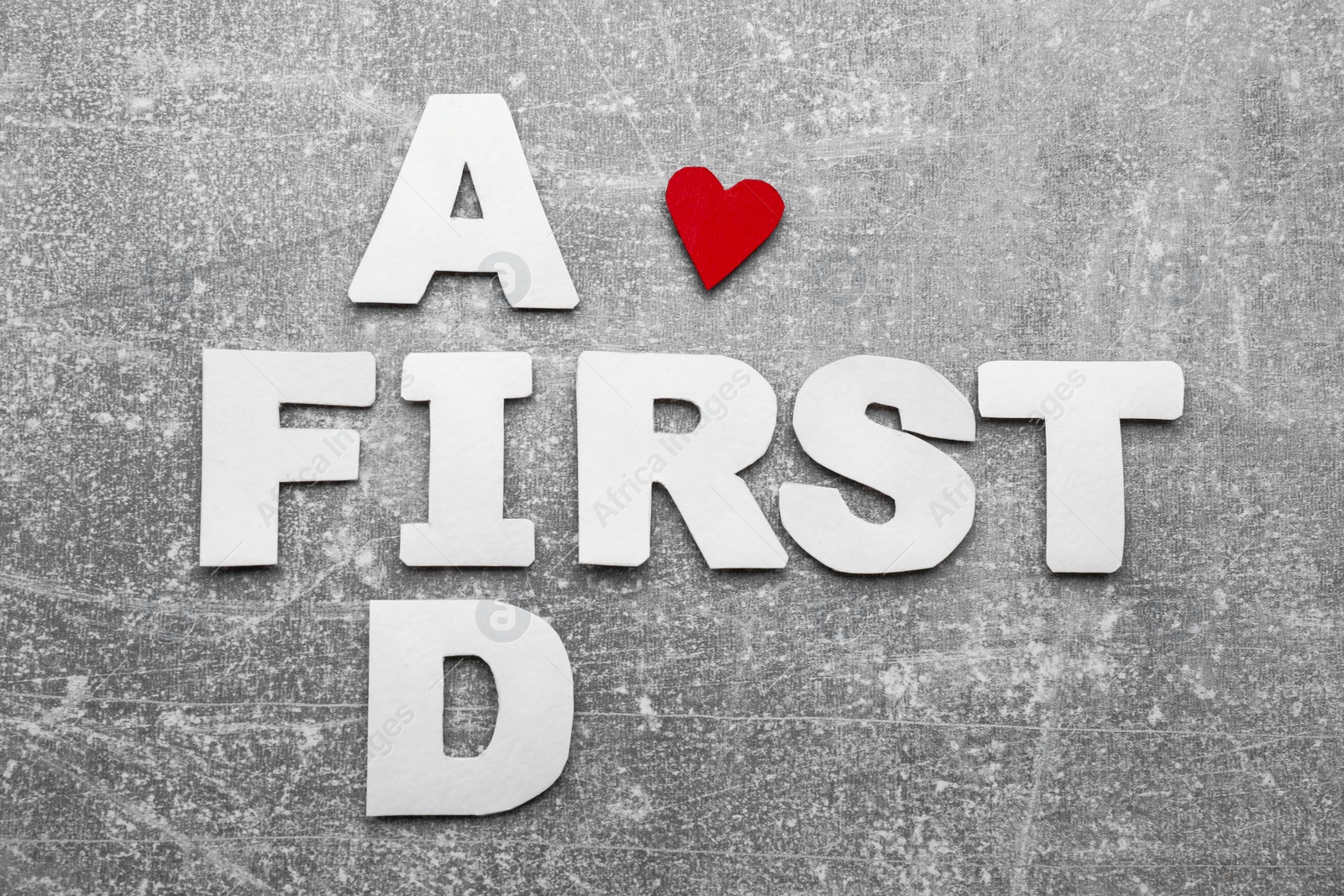 Photo of Words First Aid made of white letters and cardboard heart on light grey table, flat lay