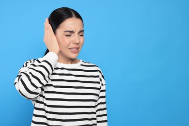 Photo of Young woman suffering from ear pain on light blue background. Space for text