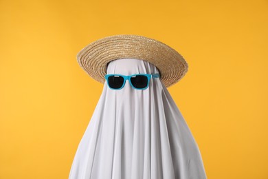 Photo of Person in ghost costume, sunglasses and straw hat on yellow background