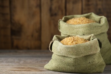 Burlap bags with uncooked bulgur on wooden table, closeup. Space for text