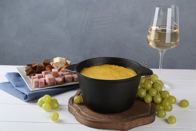 Photo of Fondue with tasty melted cheese, different products and aromatic wine in glass on white wooden table