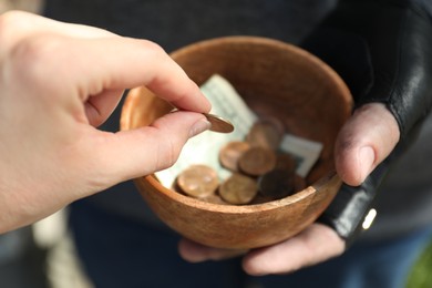 Woman giving coin to poor homeless man with bowl of donations outdoors, closeup