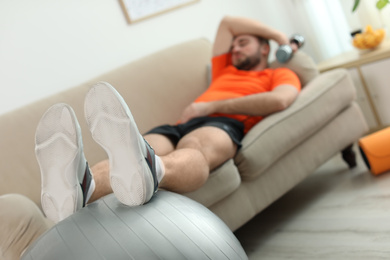 Lazy young man with sport equipment on sofa at home, focus on legs