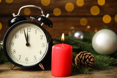 Alarm clock, burning candles and Christmas decor on wooden table, bokeh effect